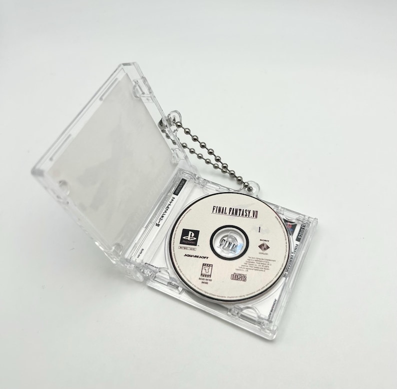 May include: A clear plastic case with a silver chain attached, holding a Final Fantasy VII video game disc. The disc is labeled "FINAL FANTASY VII" and features a PlayStation logo.