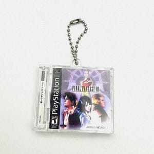 May include: A clear plastic keychain featuring a Final Fantasy VII video game cartridge. The keychain has a silver chain and the cartridge has a purple and blue background with the text "FINAL FANTASY VII" and the characters Cloud, Tifa, and Sephiroth.
