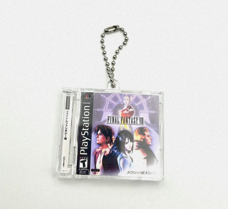 May include: A clear plastic keychain featuring a Final Fantasy VII video game cartridge. The keychain has a silver chain and the cartridge has a purple and blue background with the text "FINAL FANTASY VII" and the characters Cloud, Tifa, and Sephiroth.