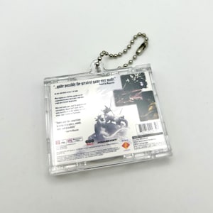 May include: A clear plastic keychain featuring the back of a video game case. The case is for the game "Final Fantasy VII" and has a quote from GameFan Magazine: "quite possibly the greatest game ever made."