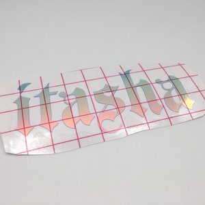 May include: A clear sheet of transfer paper with a holographic iridescent vinyl sticker of the name "Itasha" in a gothic font.