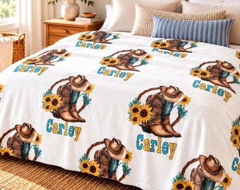 May include: A white fleece blanket featuring a repeating pattern of brown cowboy boots, tan cowboy hats, and yellow sunflowers. The name Carley is printed in a blue script font below each set of boots, hats, and sunflowers on the blanket.
