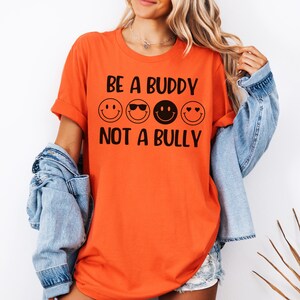 May include: Orange t-shirt with the text "Be a Buddy Not a Bully" in black lettering. Four black smiley faces are above the text.