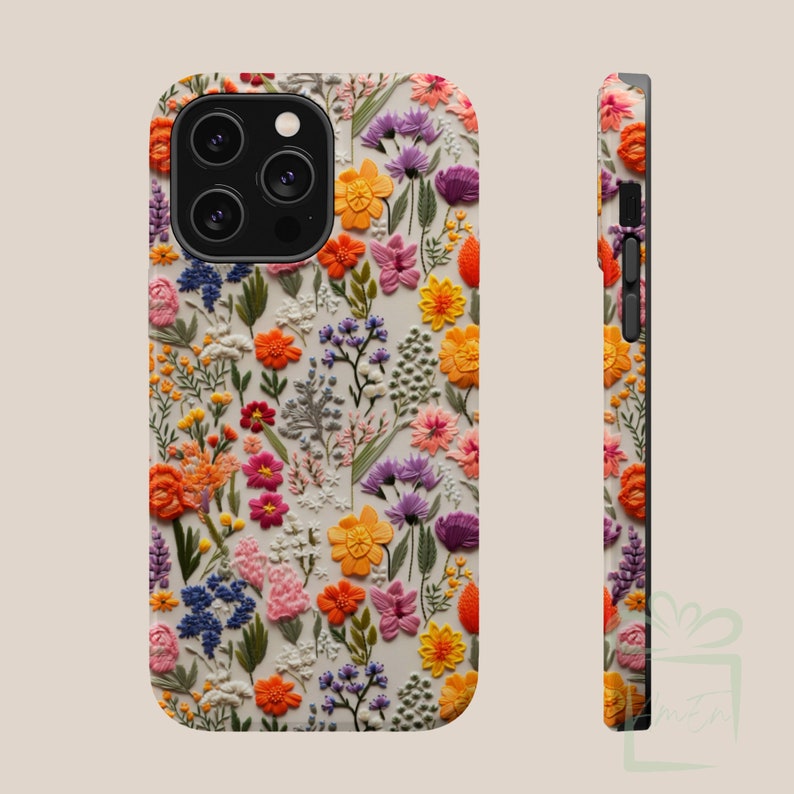 May include: A white phone case with a floral pattern. The flowers are embroidered and are in shades of pink, orange, yellow, and purple. The case has a black camera cutout and a black side.