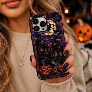 May include: A black smartphone case featuring a stained glass style design of a haunted house at night. The scene includes a large yellow full moon, a dark purple sky, a stone path, and two glowing orange jack-o'-lanterns in the foreground.