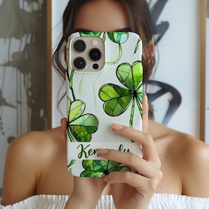 May include: A white phone case with a green four-leaf clover design. The case has a clear cutout for the camera lens and a personalized name, "Ken", printed on the bottom.
