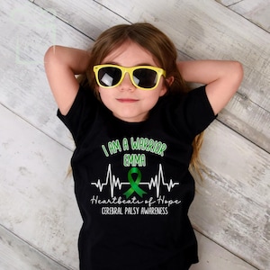 Puede incluir: Camiseta negra con una cinta verde y el texto "Soy un guerrero Emma Latidos de esperanza Conciencia de parálisis cerebral".