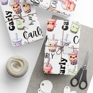 May include: White wrapping paper with a repeating pattern of cartoon bubble tea cups in various colors. The paper is tied with twine and has a tag that says "Carly". A ball of twine, scissors, and blank tags are also present.