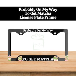 May include: A black license plate frame featuring the white text "Probably On My Way" at the top and "TO GET MATCHA" at the bottom. The frame is decorated with small, colorful illustrations of matcha drinks and bowls in shades of green and pink.