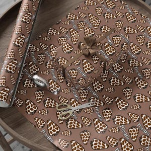 May include: Brown wrapping paper with a giraffe print and the word "Moani" in white. A wrapped gift with a brown ribbon, scissors, and tape are on the paper. The paper is on a wooden surface.