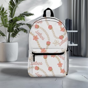 May include: White backpack with a floral pattern featuring pink flowers, white flowers, and white pearl necklaces. The text "Leilani" is repeated throughout the pattern.