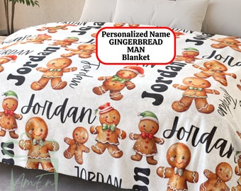 May include: White fleece blanket with a gingerbread man pattern. The blanket features multiple gingerbread men with red and green hats, brown eyes, and white icing. The name "Jordan" is repeated throughout the blanket.
