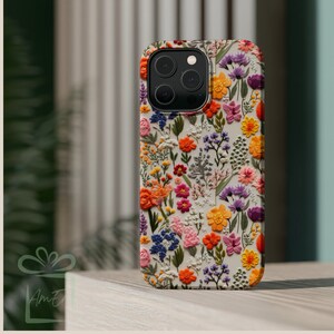 May include: A white phone case with a floral pattern. The flowers are embroidered and are in shades of pink, orange, yellow, purple, and green.