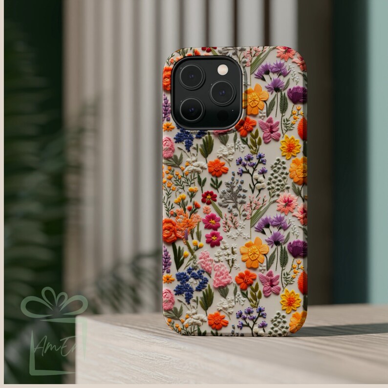 May include: A white phone case with a floral pattern. The flowers are embroidered and are in shades of pink, orange, yellow, purple, and green.