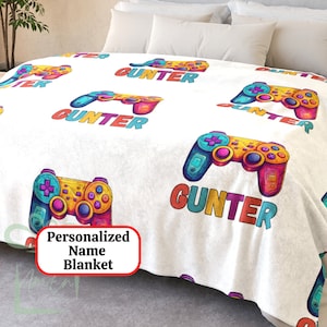 Könnte beinhalten: Eine weiße Fleece-Decke mit einem bunten Videospiel-Controller-Design und dem Namen "GUNTER", der sich über die gesamte Oberfläche wiederholt. Die Decke ist mit einem Namen personalisiert.