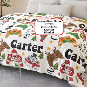 May include: White fleece blanket with a retro Christmas gamer theme. The blanket features a repeating pattern of video game controllers, Christmas trees, reindeer, and snowmen. The name "Carter" is printed in a large, bold font across the blanket. "Personalized Name Retro Christmas Gamer Blanket" is printed in a white box on the blanket.