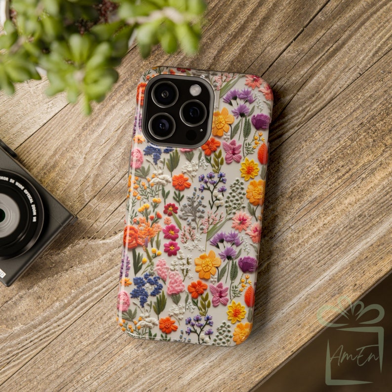 May include: A white phone case with a floral pattern. The flowers are in shades of pink, purple, orange, and yellow. The case has a raised camera bump.