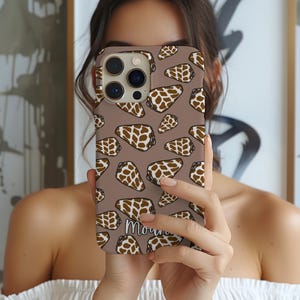 May include: A brown phone case featuring a repeating pattern of brown and white seashell illustrations. The case has a matte finish and the word "Morning" is written in a script font at the bottom.