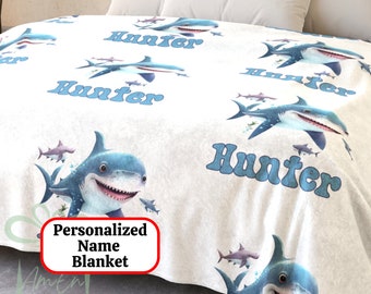 May include: White fleece blanket with a blue shark pattern and the name "Hunter" repeated throughout. The blanket is personalized with the name "Hunter".