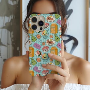 Puede incluir: Una funda de teléfono con un patrón repetido de ilustraciones de comida de dibujos animados coloridos, que incluyen sushi y hielo raspado, sobre un fondo a cuadros azul claro. La funda tiene un anillo de cámara dorado y el nombre "Emma" es visible.