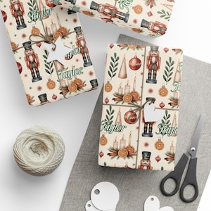Könnte beinhalten: Geschenkverpackte Geschenke mit festlichem Thema. Das Geschenkpapier zeigt ein sich wiederholendes Muster aus Nussknackern, Kerzen, Ornamenten und getrockneten Orangenscheiben. Jedes Paket ist mit Bindfaden und einem weißen Anhänger gebunden. Ein Knäuel Bindfaden und eine Schere sind ebenfalls sichtbar.
