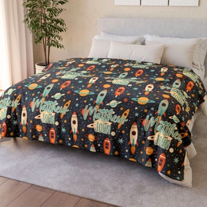May include: A black and blue fleece blanket with a space-themed pattern. The pattern features rockets, planets, stars, and the names "Matthew" and "John".