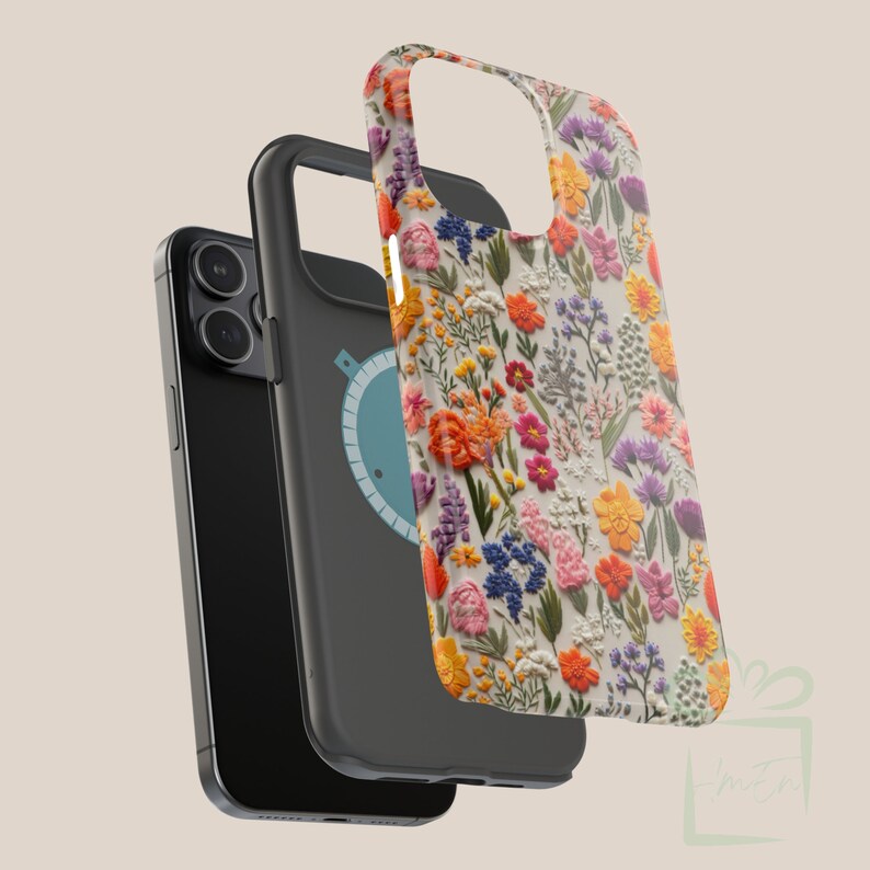 May include: A black phone case with a floral design. The case has a white background with colorful embroidered flowers. The case is shown with a black phone case with a blue circle on the back.