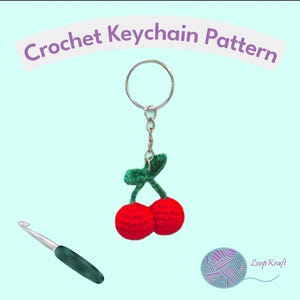 May include: A crochet keychain pattern featuring two red cherries with green stems and leaves attached to a silver metal ring. A silver crochet hook with a dark green handle is positioned below, and the text reads Crochet Keychain Pattern.