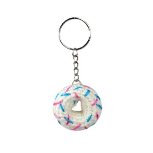 Puede incluir: Llavero de donut blanco tejido a crochet con chispas rosas y azules.