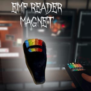May include: A black magnet shaped like an EMF reader with a rainbow-colored light display at the top and a horizontal rainbow indicator bar below. The text EMF READER MAGNET is printed in white above the object against a dark background.