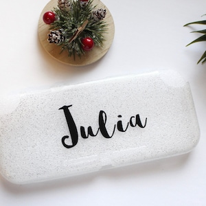 May include: White glitter cosmetic case with the name "Julia" written in black cursive lettering.