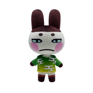 May include: A plush toy of a white rabbit with brown ears, wearing a green shirt with white markings. The rabbit has a white face with pink cheeks and a slightly frowning expression.