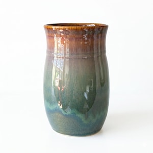 May include: A handcrafted ceramic vase with a glossy finish. The vase transitions from a rich brown at the rim to a deep teal and blue at the base. The smooth, curved shape is ideal for displaying flowers or as a decorative piece.