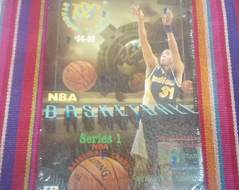 May include: A pack of 1994-95 NBA Basketball trading cards, featuring a basketball player in a yellow and blue uniform with the word "Indiana" on the front. The pack is labeled "Series 1" and features a basketball with the word "Spalding" on it.