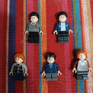 May include: Six Lego minifigures of characters from the Harry Potter series. The figures are wearing various outfits, including school uniforms and casual wear. The figures are on a striped red, orange, and yellow background.