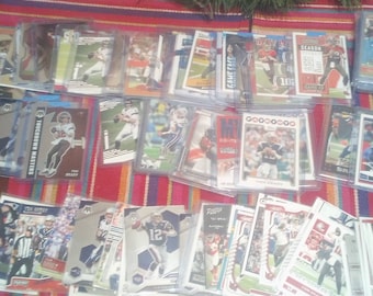 Könnte beinhalten: Eine Sammlung von Football-Sammelkarten mit verschiedenen Spielern und Teams. Die Karten sind in Reihen auf einer bunten gestreiften Oberfläche angeordnet. Einige der Karten haben eine silberne Folienveredelung und zeigen den Text "TOUCHDOWN MASTERS" und "GAME FACE".