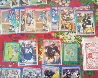 Könnte beinhalten: Eine Sammlung bunter Football-Sammelkarten mit verschiedenen Spielern und Teams. Die Karten sind in Reihen auf einer rot-grünen gemusterten Oberfläche angeordnet. Die Karten zeigen eine Vielzahl von Spielern, darunter Mel Gray, Johnny Holland und Pat Terrell. Die Karten zeigen auch den Text "1990 Rookie" und "Super Bowl Trivia".