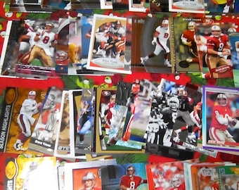 Könnte beinhalten: Eine Sammlung von Sammelkarten mit dem Footballspieler Steve Young. Die Karten sind in verschiedenen Farben und Designs gehalten, einige mit goldenem Hintergrund, andere mit silbernem Hintergrund. Die Karten sind in einem Raster auf einer rot-grünen Oberfläche angeordnet.