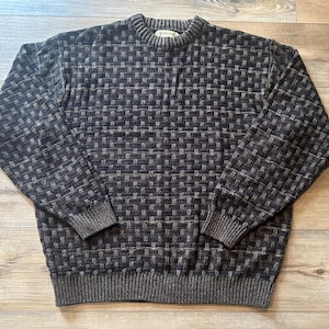 May include: A dark gray sweater with a woven basket weave pattern. The sweater has a crew neck, long sleeves, and ribbed cuffs and hem. The overall color is a mix of dark gray and lighter gray threads.