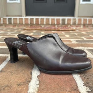 May include: A pair of dark brown leather mules with a high heel. The shoes have a pointed toe and a slip-on design. The heels are approximately 3 inches tall. The brand name "Modern Tootsies" is visible on the insole.