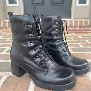 May include: A pair of black leather lace-up ankle boots featuring a square toe, a block heel, and a thick lug sole. The boots have silver-toned metal eyelets and hooks for the black laces, with a pull tab at the back of the ankle collar.