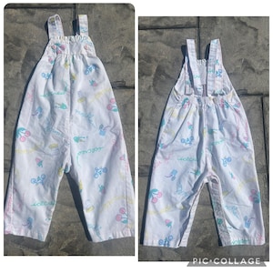May include: White overall pants with a colorful pattern of cherries, ice cream, bicycles, and the word "ice cream" in a script font. The overalls have adjustable straps and button closures.