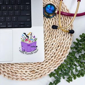 May include: A laptop with a sticker featuring a purple book with the word "Fantasy" and the text "Cool nurses read." The sticker has floral and fantasy elements. A stethoscope and greenery are also visible.