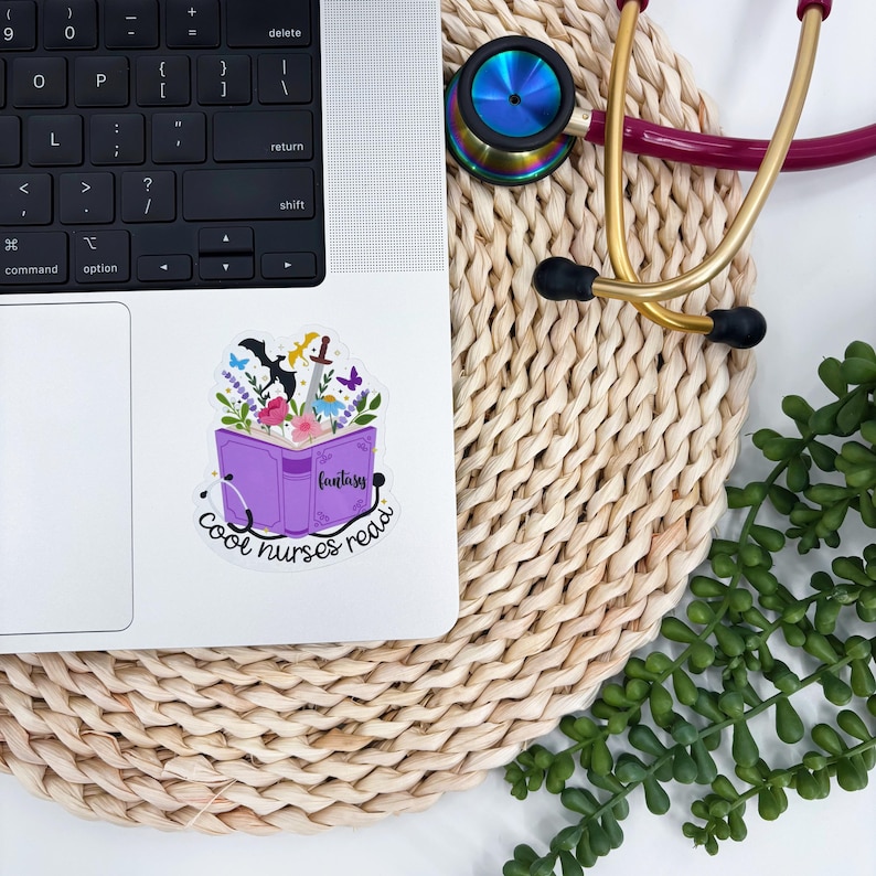 May include: A laptop with a sticker featuring a purple book with the word "Fantasy" and the text "Cool nurses read." The sticker has floral and fantasy elements. A stethoscope and greenery are also visible.