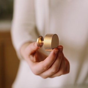 May include: A gold-toned cabinet knob with a ridged design. The knob has a round base and a small, round stem.