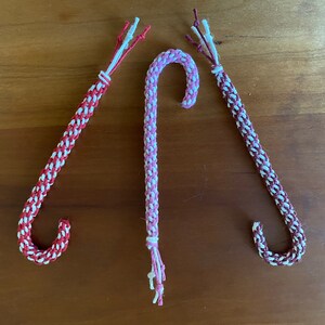 Könnte beinhalten: Drei handgefertigte Zuckerstangen-Ornamente, eine rosa und weiß, eine rot und weiß und eine burgunderrot und weiß.