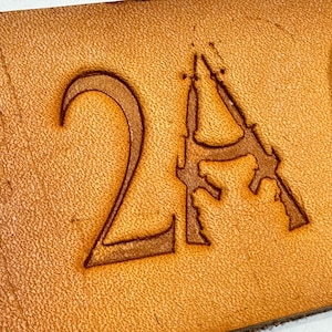 Op de afbeelding: Een close-up van een leer ambachtelijk project met het nummer "2A" gestempeld in het leer. De stempel is zichtbaar op de achtergrond.
