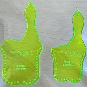 Op de afbeelding: Twee groene plastic sjablonen voor leerbewerking. De grotere sjabloon is gelabeld "Hunter Template" en de kleinere sjabloon is gelabeld "Trapper Template".