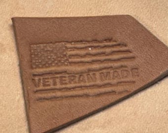 Könnte beinhalten: Ein braunes Lederstück mit einer amerikanischen Flagge und dem geprägten Text "Veteran Made".