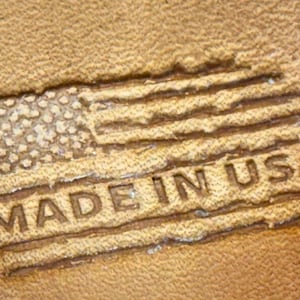 May include: A close-up of a brown leather surface with a stamped image of the American flag and the text "MADE IN USA".